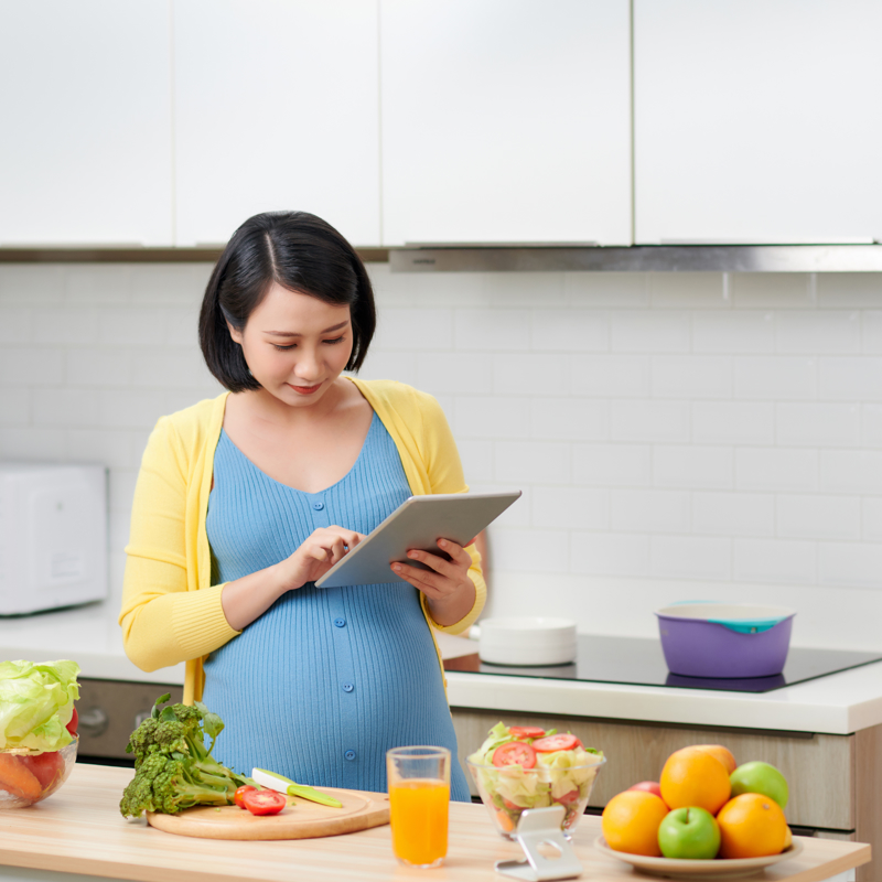 Pregnant woman cooking and preparing food from recipe