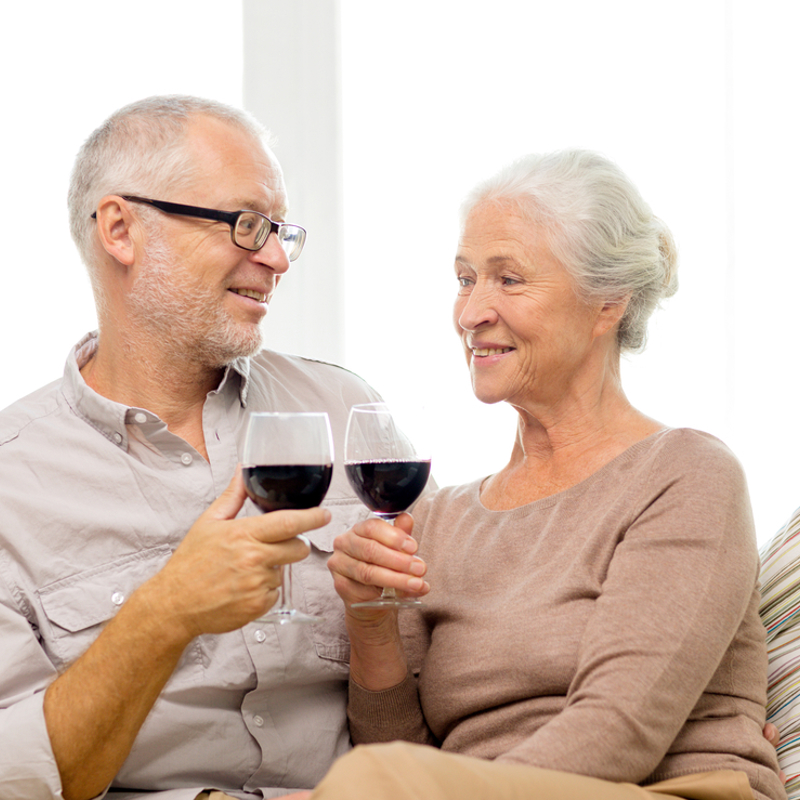An older man and woman sitting on the sofa drinking red wine