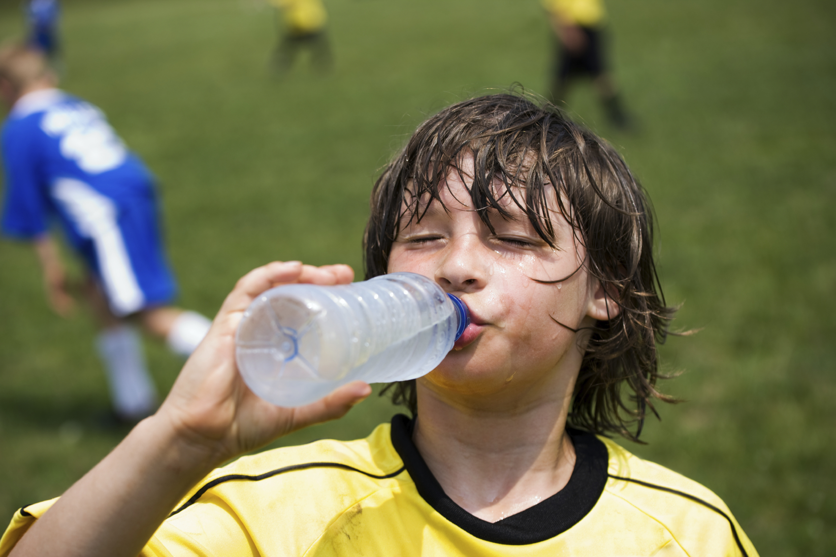 Boy drinking from a bottle of cold water during a football match loading=