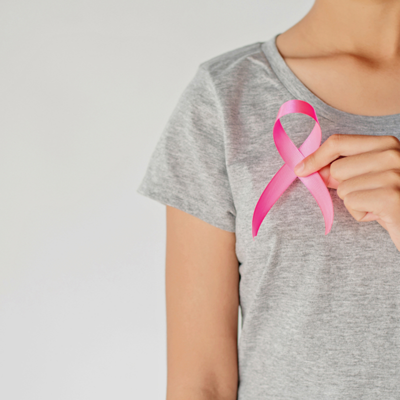 A woman holding up a pink ribbon to her chest
