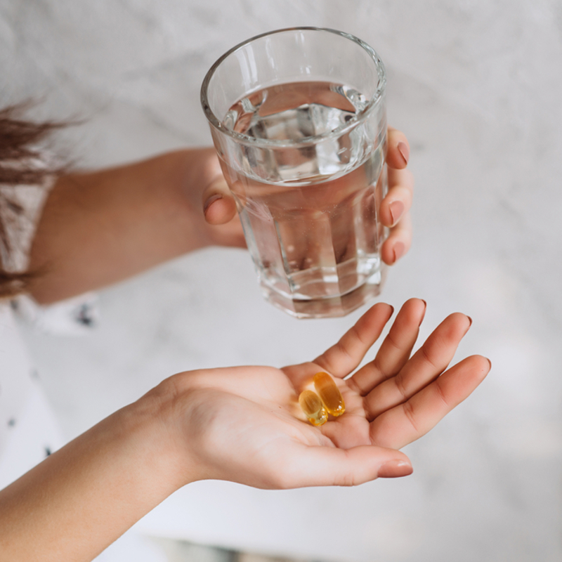 A woman holding supplements in her hand and a glass of water
