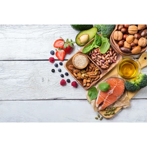 A selection of foods that contain healthy fats on a white table, including avocado, salmon, nuts and oil loading=