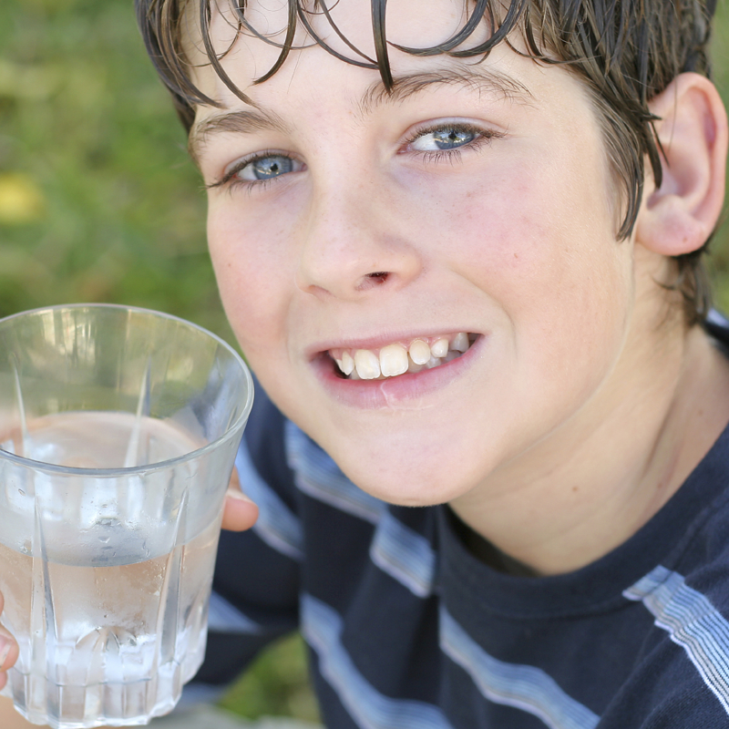 A boy who has been active drinking a glass of water