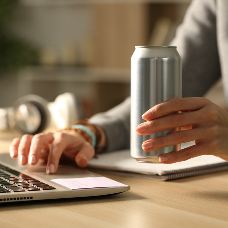 A teenager drinking an energy drink while working on laptop