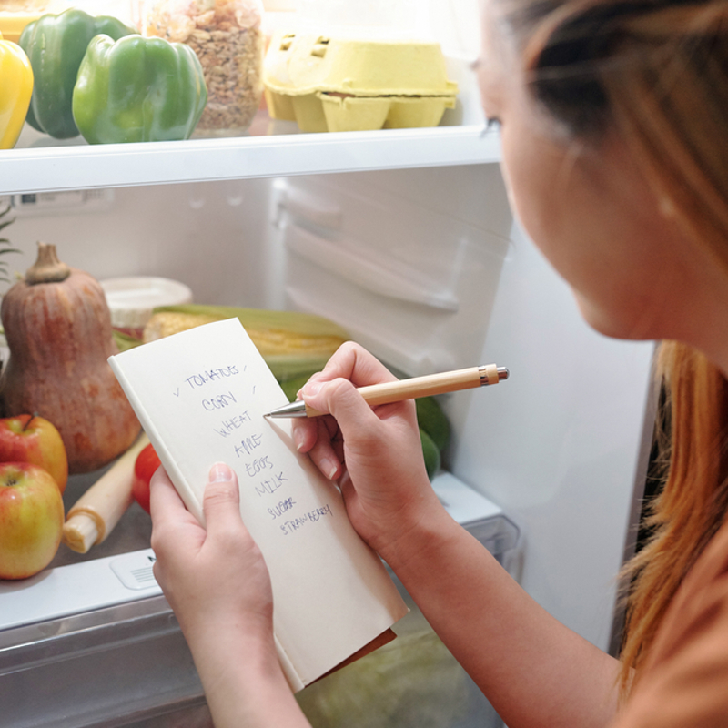 Woman looking in the fridge and making a shopping list