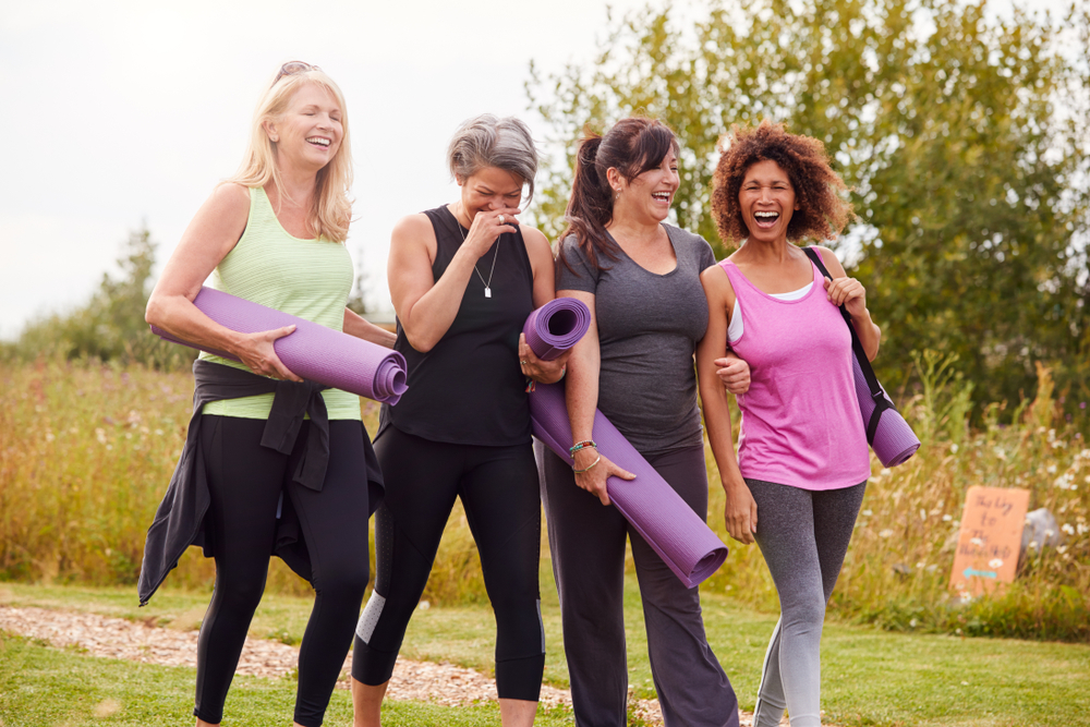 A diverse group of happy ladies, carrying yoga mats through a garden loading=