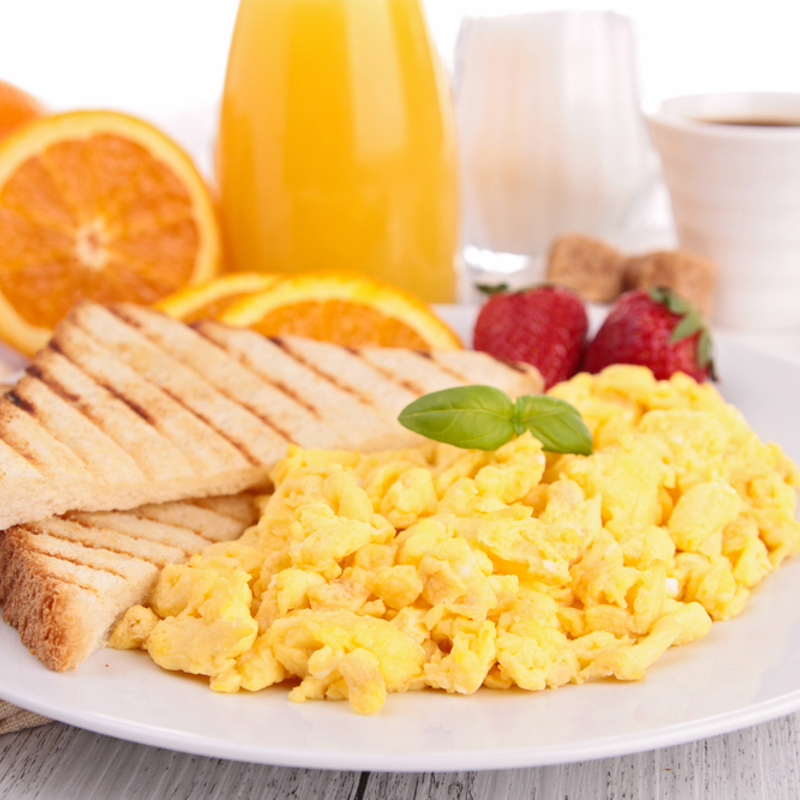 Scrambled eggs and toast next to a glass of orange juice and a hot drink