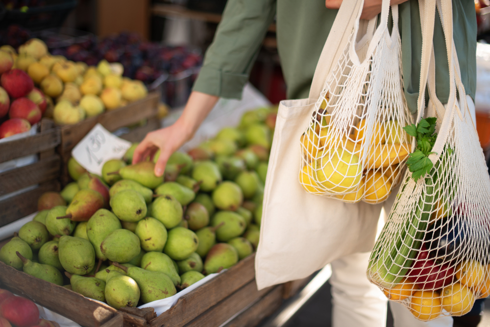 A photo of a woman holding a string bag, gathering citrus fruit and putting it in the bag loading=