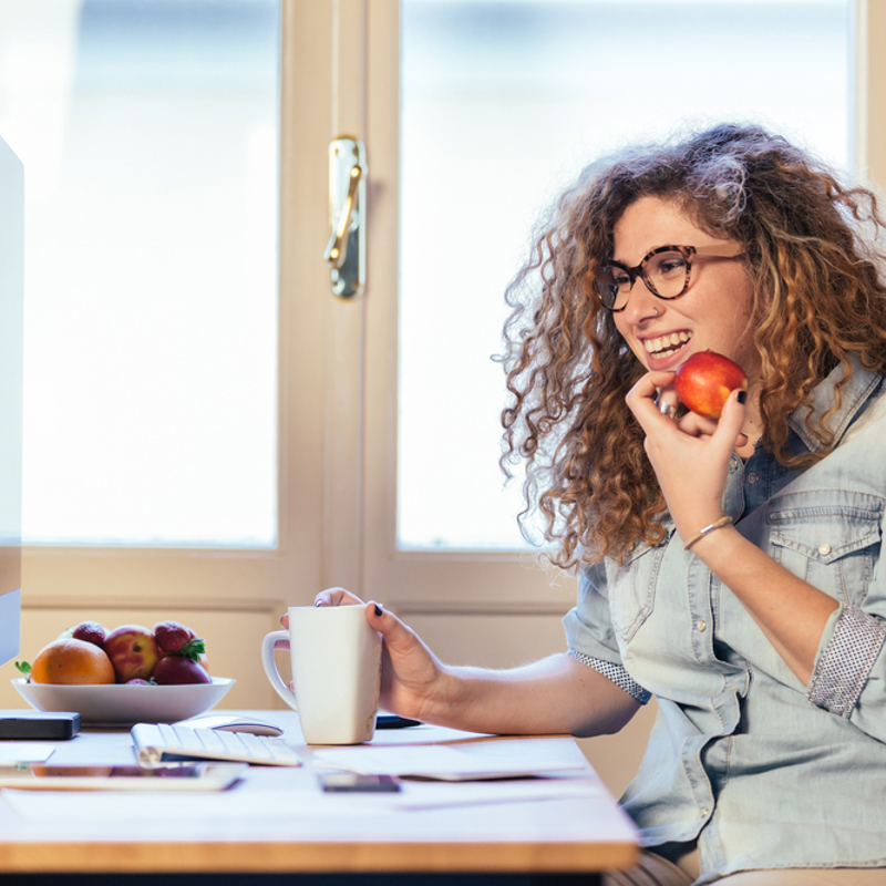 A woman snacking on an apple while working at a computer