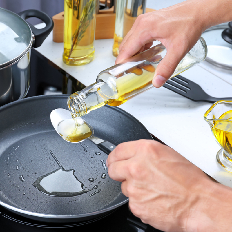 An adult measuring cooking oil on a spoon to add to a frying pan
