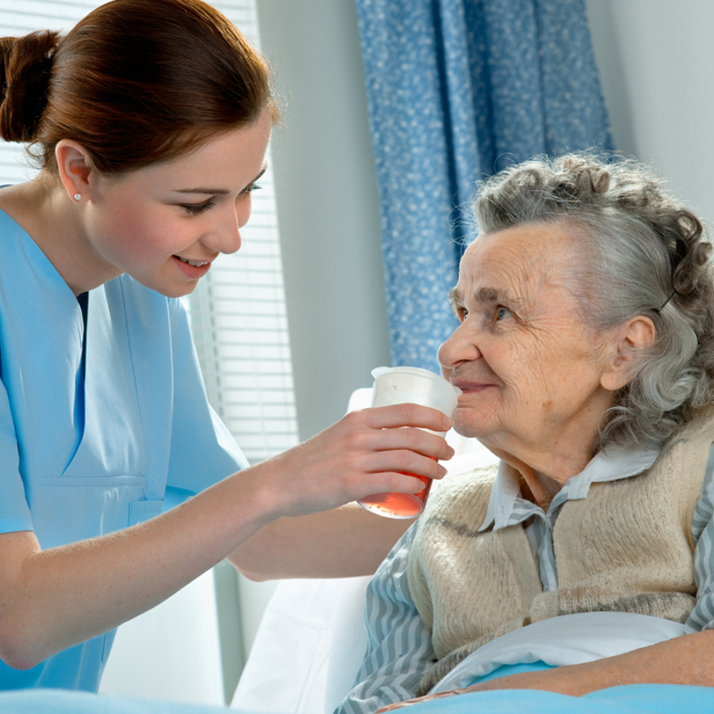 A nurse helping an older woman drinking water in hospital