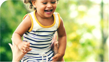 A young, happy girl being lifted up by an adult in a garden loading=