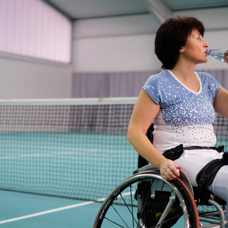 Woman in a wheelchair playing tennis drinking water from a bottle