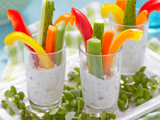 Three glasses filled with a low fat dip and vegetable sticks, including celery and red and yellow peppers