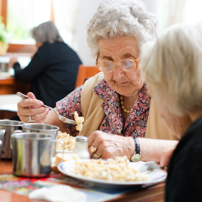 Two older women in a residential home eating a meal together